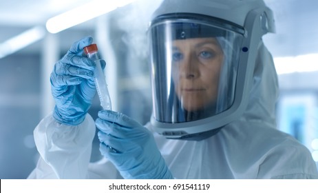 Medical Virology Research Scientist Works in a Hazmat Suit with Mask, Inspects Test Tube with Isolated Virus String from Refrigerator Box. She Works in a Sterile High Tech Laboratory Facility.