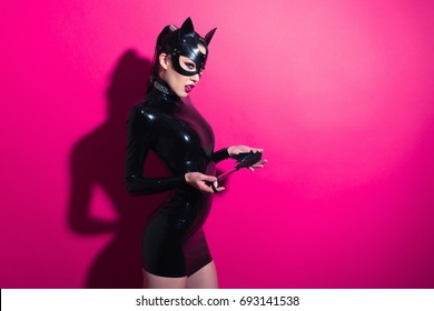 グラマー ラテックス ドレス、襟、bdsm 黒革フェチ猫マスク ポーズ ホット ピンク背景でファッション メイクと美しい支配的なブルネット ヴァンプ愛人少女
