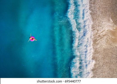 トルコのオルデニズの透明なターコイズ ブルーの海でピンクの水泳リングで泳いでいる若い女性の空撮。女の子と夏の海の風景、美しい波、晴れた日の紺碧の水。ドローンからのトップ ビュー