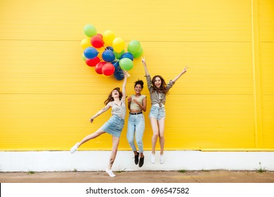 Foto van jonge gelukkige vrouwenvrienden die zich over gele muur bevinden. Veel plezier met ballonnen.