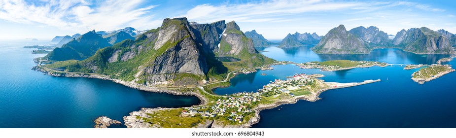 Luftpanoramablick des traditionellen Fischerdorfes Reine im Lofoten-Archipel in Nordnorwegen mit blauem Meer und Bergen während des sonnigen arktischen Sommers
