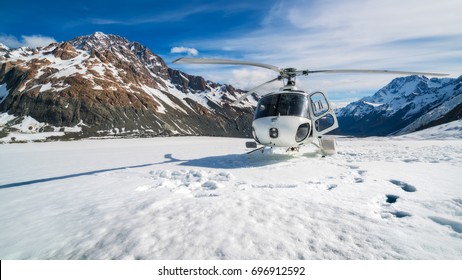 ニュージーランド、マウント・クックのタスマン氷河の雪山に着陸するヘリコプター。マウント クックのヘリコプター サービスでは、遊覧飛行、氷河への着陸、緊急救助を行っています。