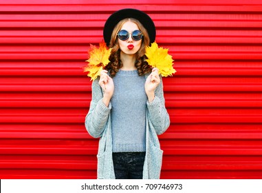 Mujer de retrato de otoño de moda con hojas de arce amarillas sobre un fondo rojo