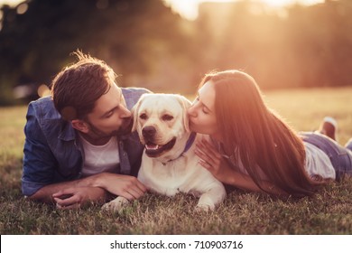 Hermosa pareja romántica se divierte con su perro labrador retriever al aire libre. Acostado sobre una hierba verde durante la puesta de sol.