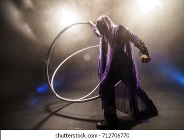 Fairy-tale character assassin in a purple cloak with a hood with two large cross wheel