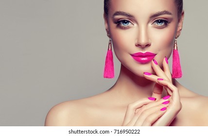 Beautiful model girl with pink fuchsia manicure on nails . Fashion makeup and cosmetics . Large earrings tassels jewelry Magenta color .