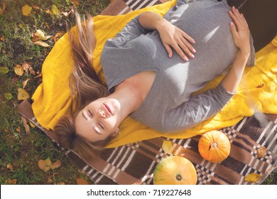  pregnant woman 30-35 years old relaxing and lying on a picnic. Autumn harvest. pumpkins, yellow knitted plaid