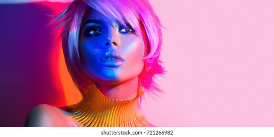 Modna manekenka v pisanih močnih lučeh, portret čudovite deklice s trendovskim ličenjem, frizuro. Umetniško oblikovanje disko plesalke, barvit make up. Na barvitem živo roza ozadju,