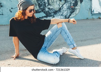 Modelo con camiseta negra lisa, jeans boyfriend, zapatillas y gafas de sol hipster posando contra la pared de la calle, estilo de ropa urbana adolescente, maqueta para la tienda de impresión de camisetas