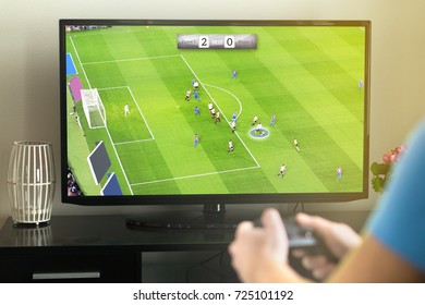 Un giovane che esce e gioca a un videogioco immaginario di calcio o football con console e TV. Tiene il controller in mano. Divertente attività per il tempo libero.