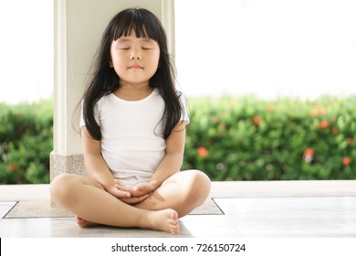 Asian children cute or kid girl sit for meditation with peace and relax in garden pavilion at temple or church and wearing white dress with sunlight on white with space