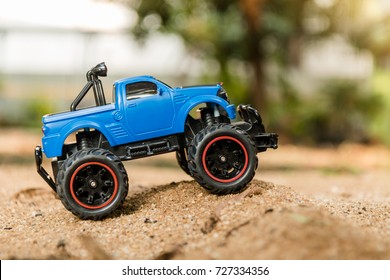 Blauer ferngesteuerter Geländewagen (RC-Truck) steht auf einer Sanddüne. Das Spielzeug ist etwas verstaubt, da Kinder damit gespielt haben.