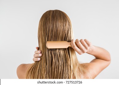 グレイの背景にシャワーを浴びた後、濡れたブロンドの髪をブラッシングする櫛を持つ女性。健康できれいな髪をケアします。ビューティー サロンのコンセプトです。