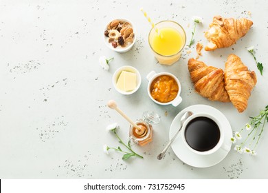 Continentaal ontbijt van bovenaf vastgelegd (bovenaanzicht, platliggend). Koffie, jus d'orange, croissants, jam, honing en bloemen. Grijze stenen werkblad als achtergrond. Lay-out met vrije tekst (kopie) ruimte.