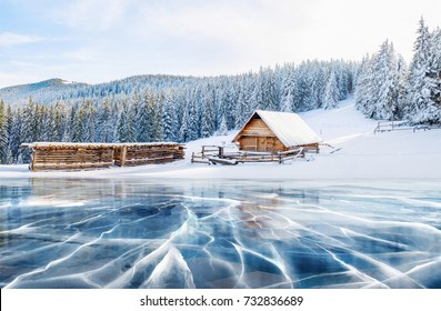 Grietas en la superficie del hielo azul. Lago congelado en las montañas de invierno. Está nevando. Las colinas de pinos y cabaña en las montañas. Niebla misteriosa. Cárpatos Ucrania