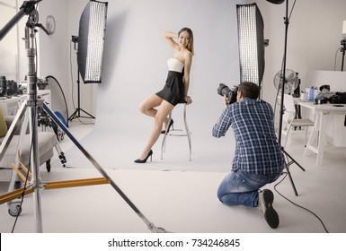 Professionelles Fotoshooting im Studio: ein schönes junges Model lächelt und posiert; Der Fotograf fotografiert mit einer Digitalkamera