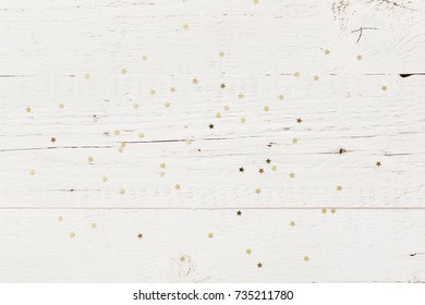 Small golden stars confetti on white retro wooden background.