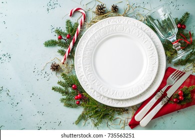 Elegante diseño de mesa navideña capturado desde arriba (vista superior, plano). Plato blanco vacío, vidrio, cubiertos, bastón de caramelo y decoraciones. Diseño de fondo con espacio de texto libre (copia).