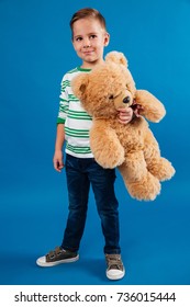 Porträt in voller Länge eines lächelnden kleinen Jungen, der Teddybär hält und weg lokalisiert über blauem Hintergrund schaut