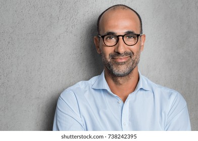 Portrait of a mature businessman wearing glasses on grey background. Happy senior latin man looking at camera isolated over grey wall with copy space. Close up face of happy successful business man.