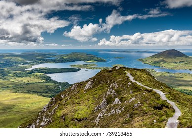 The hiking trail at the top of Diamond Hill in Connemara National Park, Ireland. Behind, the sun plays with the clouds reflected in the sea.