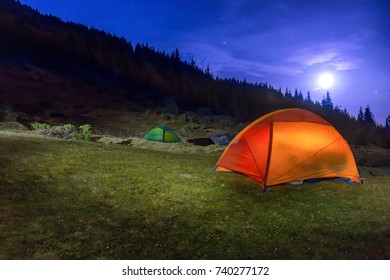 Zwei beleuchtete orange und grüne Campingzelte unter Mond, Sterne in der Nacht
