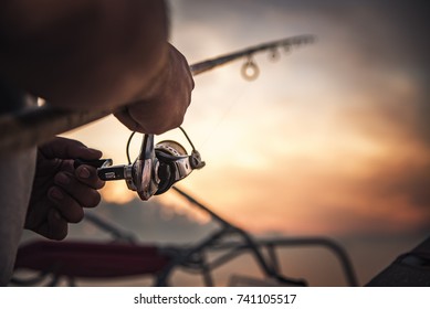 釣り竿の車輪の接写、美しい日の出を背景に釣りをする男性