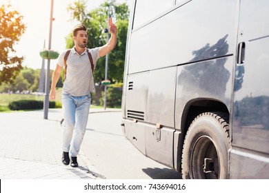 Der Typ rennt hinter dem abfahrenden Bus her. Er hat den Bus verpasst und versucht, ihn einzuholen. Er rennt hinter einem modernen schwarzen Bus her und wedelt mit der Hand, um ihn anzuhalten.