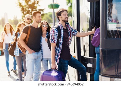 Eine Gruppe von Touristen bereitet sich darauf vor, in den Bus einzusteigen. Der Typ mit dem Mädchen geht in den Bus und bringt ihr Gepäck herein. Das Mädchen geht zuerst. Dahinter wartet eine Gruppe Touristen.