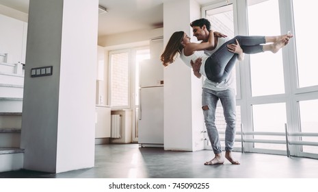 自宅でロマンチックなカップル。魅力的な若い女性とハンサムな男性が一緒に過ごす時間を楽しんでいます。情熱的なカップルは、パノラマの窓のある明るいモダンなキッチンで踊っています。
