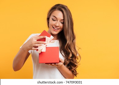 Retrato de una chica sonriente feliz abriendo una caja de regalo aislada sobre fondo amarillo