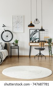 Moqueta redonda blanca en la habitación de un adolescente con lámparas encima de una silla en el escritorio y una bicicleta en la cabecera de la cama