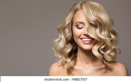 Blonde woman with curly beautiful hair smiling on gray background. 