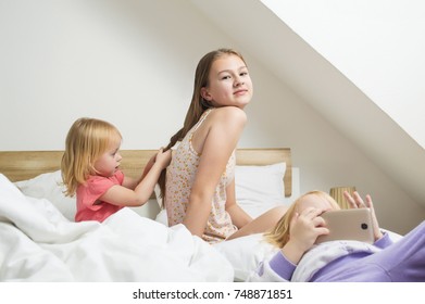 morning games on the bed, combing, the younger sister makes a hairdo for her older sister. A small bright bedroom bathed in morning light. Saturday morning Morning in a large family