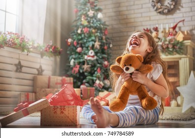 Schöne Ferien! Nettes kleines Kinderöffnungsgeschenk nahe Weihnachtsbaum. Das Mädchen lacht und genießt das Geschenk.