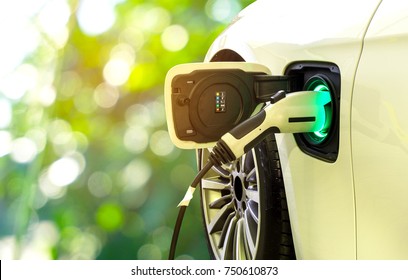 EV-Auto oder Elektroauto an der Ladestation mit eingestecktem Netzkabel auf unscharfer Natur mit weichem Lichthintergrund. Umweltfreundliches alternatives Energiekonzept