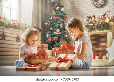Frohe Weihnachten und schöne Feiertage! Fröhliche süße Kindermädchen, die Geschenke öffnen. Kinder, die Pyjamas tragen, haben morgens Spaß in der Nähe des Baumes. Liebevolle Familie mit Geschenken im Zimmer.