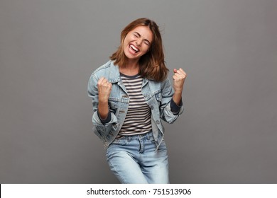 Potret seorang gadis remaja yang ceria mengenakan jaket denim merayakan kesuksesan sambil menari terisolasi di atas latar belakang abu-abu