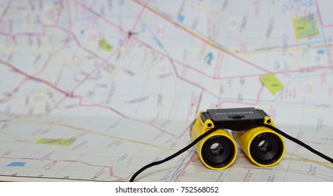 plastic toy binocular (with wording to identify what it is on top) in vivid yellow and black with blurred map as background