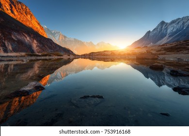 Hermoso paisaje con rocas altas con picos iluminados, piedras en lago de montaña, reflejo, cielo azul y luz solar amarilla al amanecer. Nepal. Increíble escena con las montañas del Himalaya. Himalaya