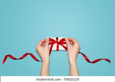 Weihnachtsferien Zusammensetzung. Neujahrsgeschenk in der weißen Box mit rotem Band in den weiblichen Händen auf der flachen Hintergrund-Draufsicht des blauen Hintergrunds mit Kopierraum für Ihren Text