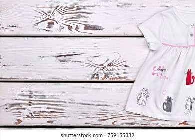Baby girl cats cartoon dress. Newborn girl short sleeve white dress on white wooden background, copy space.