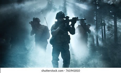 Silhouette des voll ausgestatteten Soldaten, der sich durch Smokey Forest mit schussbereitem Gewehr bewegt. Aufklärung Militäroperation. Trupp bewegt sich hinter ihm. Dunkle und kalte Umgebung.