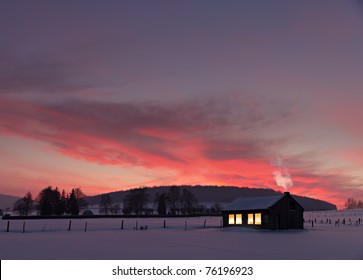 casita con ventanas decoradas iluminadas frente a una puesta de sol de invierno en la nieve