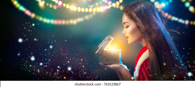 Wanita Musim Dingin Natal membuka kotak Hadiah Natal ajaib. Peri. Adegan Tahun Baru dan Natal yang Indah, Model Busana Cantik Gadis Dengan Kotak Hadiah di malam hari. Bintang dan cahaya Sihir Liburan