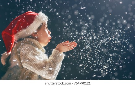 Wesołych Świąt i szczęśliwego Nowego Roku! Mała dziewczynka dmucha na śnieg. Dziecko bawi się na świeżym powietrzu. Portret dziecka na ciemnym tle.