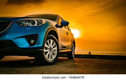Blue compact SUV car with sport and modern design parked on concrete road by the sea at sunset. Environmentally friendly technology. Business success concept.