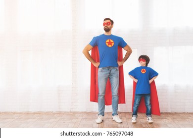 Hai cha con trong bộ đồ xanh đỏ của các siêu anh hùng. Trên mặt họ đeo khẩu trang và mặc áo mưa. Họ đang tạo dáng trong một căn phòng sáng sủa.