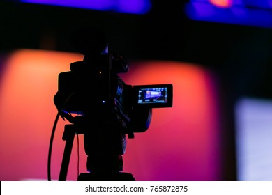 Silhouette of a video camera capturing an event on stage. Live streaming tv. Breaking news. News event. Story. Reporter. Live Broadcast