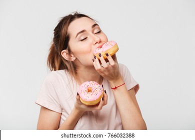 Close-up portret van een tevreden mooi meisje dat donuts eet geïsoleerd op witte achtergrond